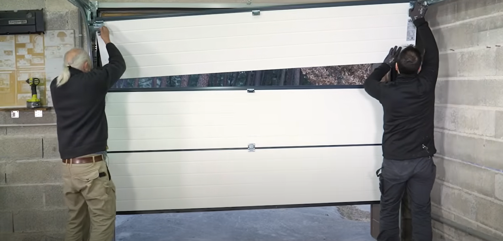 Technician repairing a white sectional garage door with a manual tool.