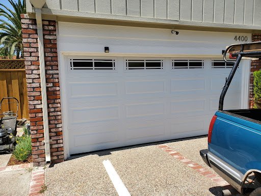 Technician repairing a white sectional garage door with a manual tool.