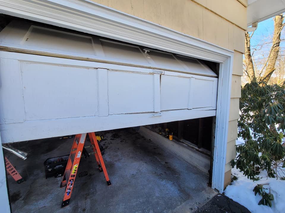 Technician repairing a white sectional garage door with a manual tool.